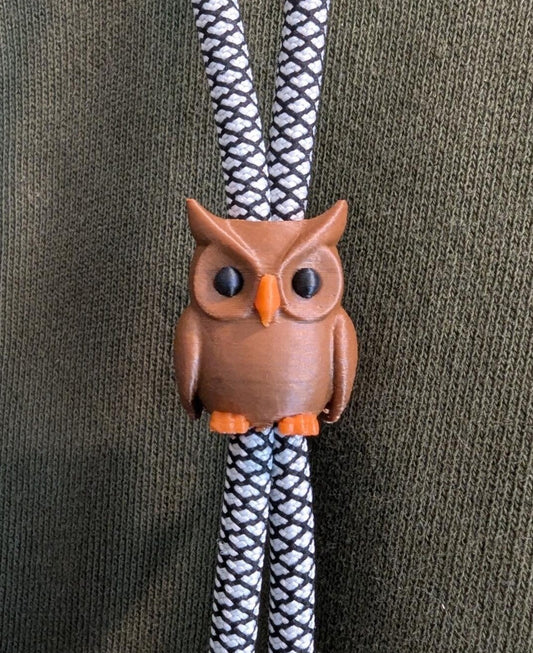 Owl charm on a braided black and white cord against a green fabric background
